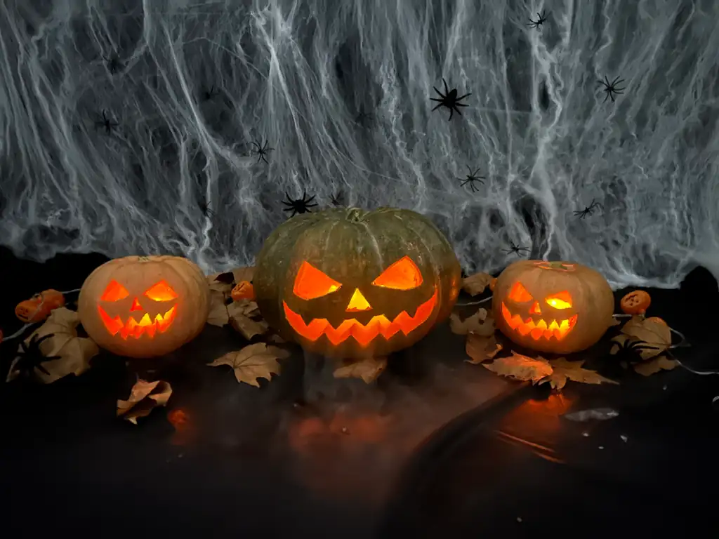 Tres calabazas talladas e iluminadas sobre una mesa, con niebla de hielo seco a ras de la superficie